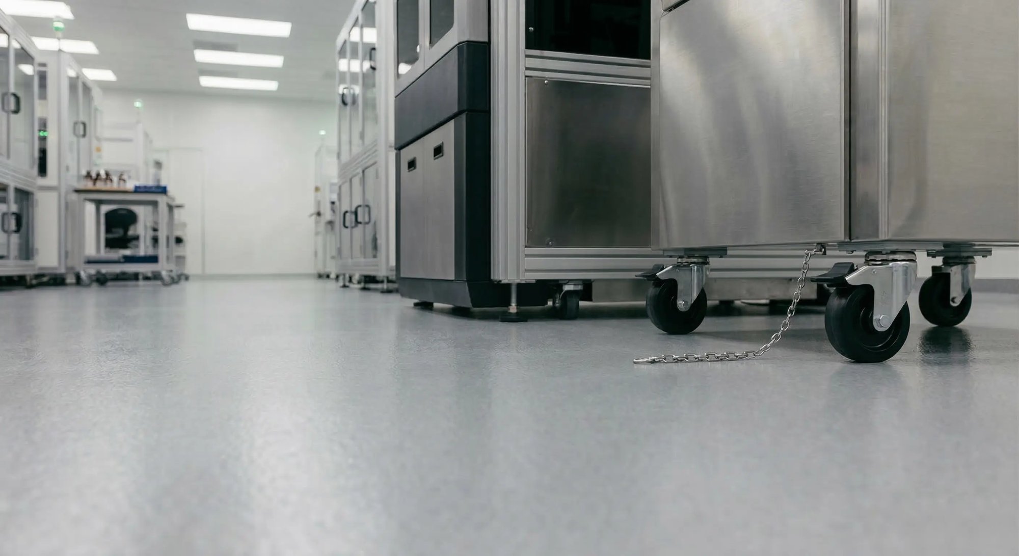 A stainless steel cart with an ESD grounding chain trailing on a conductive cleanroom floor in an electronics manufacturing facility.