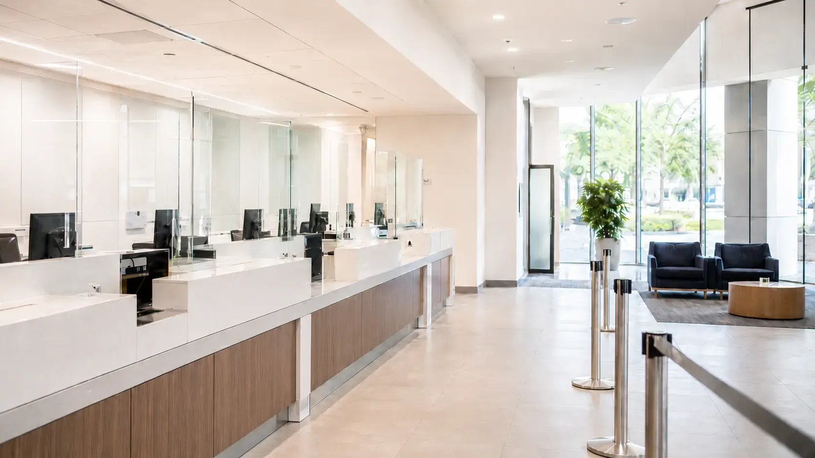A bright, modern bank lobby with a glass-paneled teller counter, wood accents, and a waiting area near floor-to-ceiling windows.