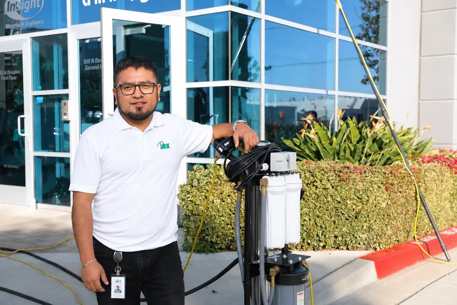 An iNX technician stands beside a water-fed pole window cleaning system outside a commercial office building.