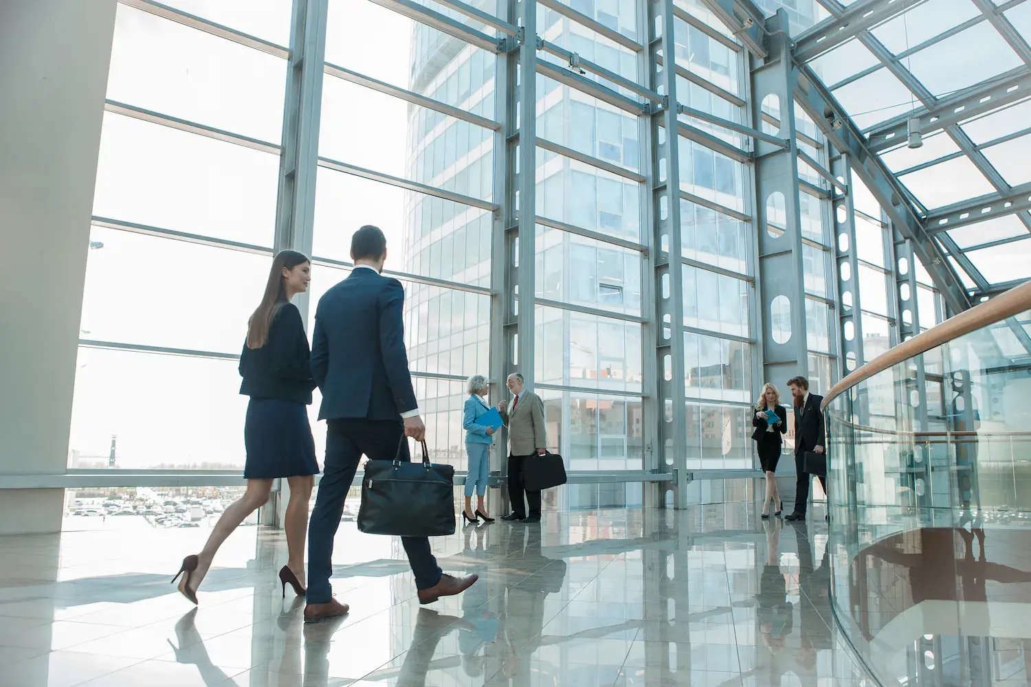 Business professionals walking through a bright, modern commercial building lobby with floor-to-ceiling windows and polished floors.Business professionals walking through a bright, modern commercial building lobby with floor-to-ceiling windows and polished floors.