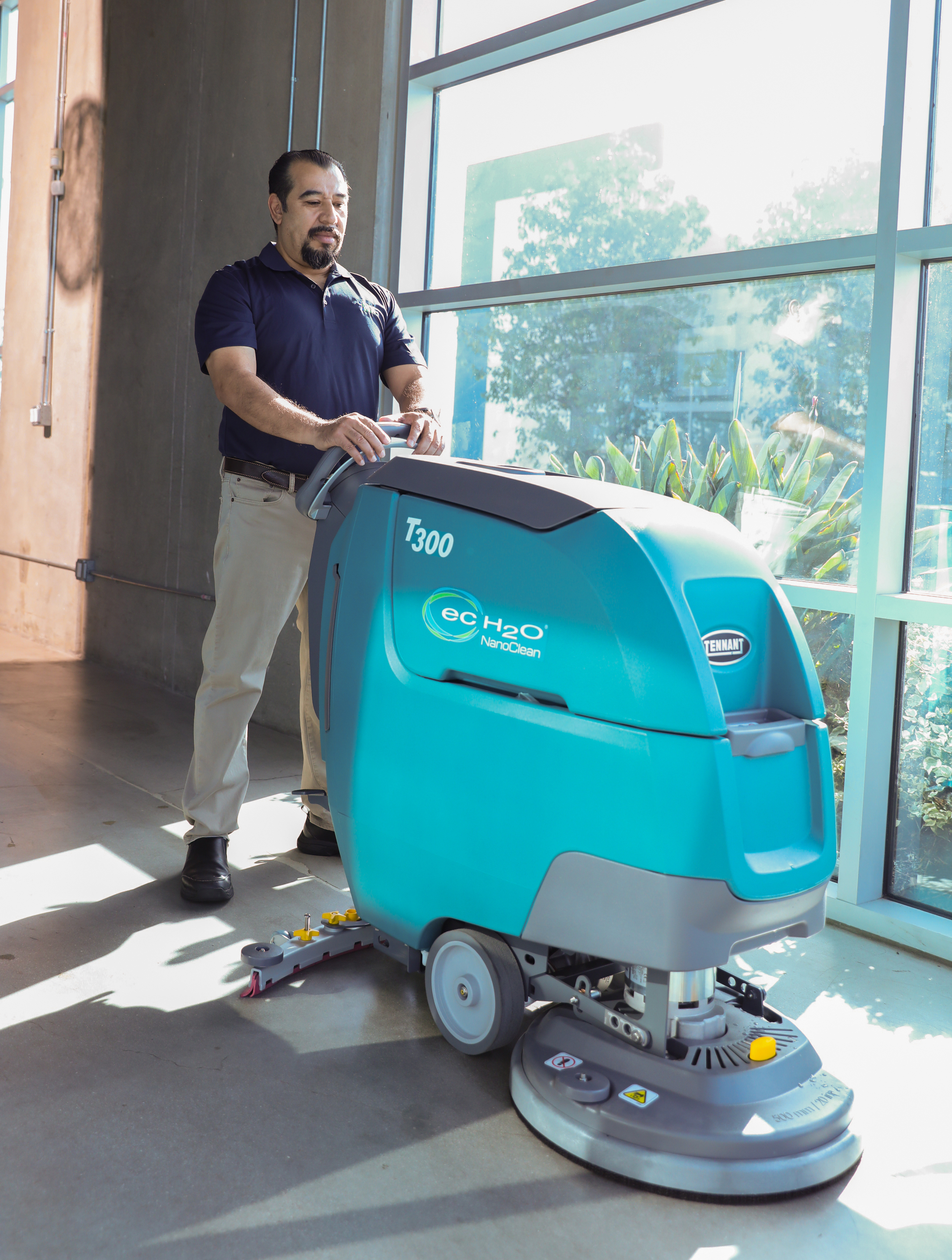 iNX technician operating a Tennant T300 walk-behind auto scrubber on a commercial floor.