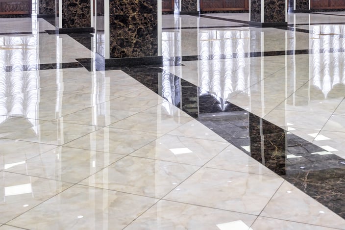 High-gloss polished marble floor in a commercial lobby, reflecting light across the tile surface.