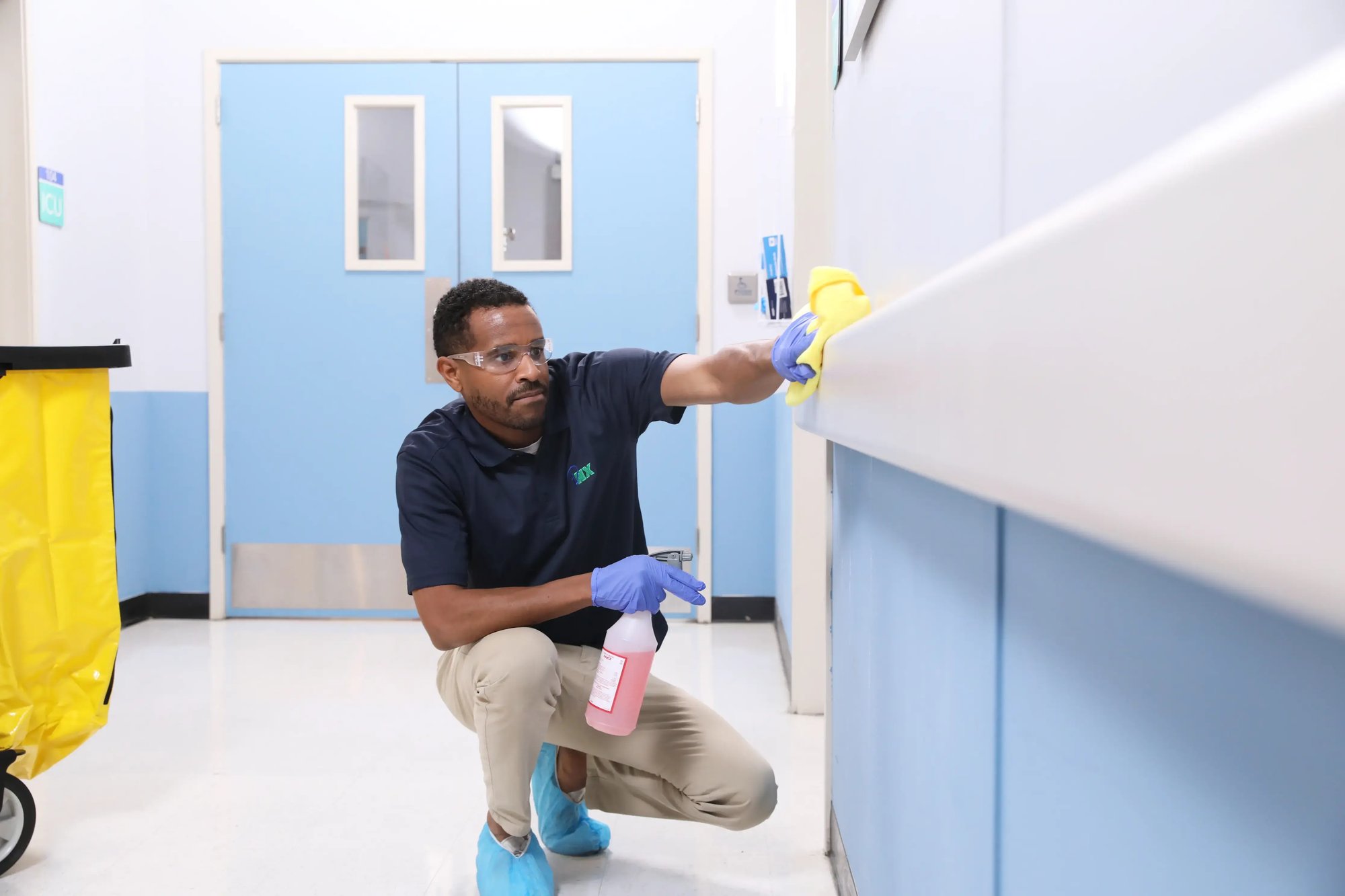 iNX technician disinfecting a high-touch surface in a healthcare facility corridor.